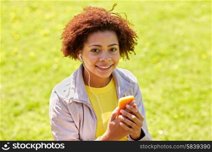 technology, lifestyle and people concept - happy african american young woman or teenage girl with smartphone and earphones listening to music in summer park