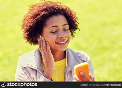technology, lifestyle and people concept - happy african american young woman or teenage girl with smartphone and earphones listening to music in summer park