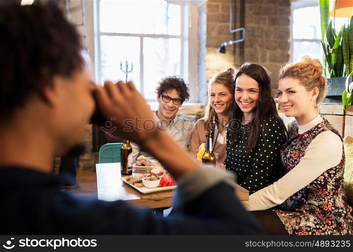 technology, lifestyle and people concept - happy friends with camera photographing at bar or cafe