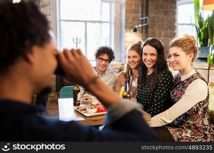 technology, lifestyle and people concept - happy friends with camera photographing at bar or cafe