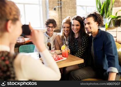 technology, lifestyle and people concept - happy friends with camera photographing at bar or cafe. friends with camera photographing at bar or cafe