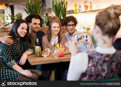technology, lifestyle and people concept - happy friends with smartphone photographing at bar or cafe