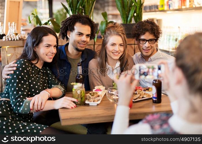 technology, lifestyle and people concept - happy friends with smartphone photographing at bar or cafe. friends with smartphone photographing at cafe