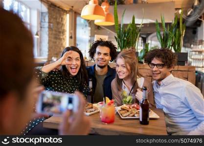 technology, lifestyle and people concept - happy friends with smartphone photographing at bar or cafe. friends with smartphone photographing at cafe