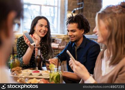 technology, lifestyle and people concept - happy friends with smartphones taking picture of food at bar or cafe. friends with smartphones and food at bar or cafe