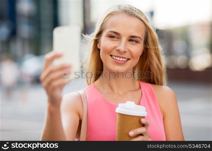technology, lifestyle and people concept - happy smiling young woman with coffee and smartphone taking selfie on city street. woman with coffee taking selfie by smartphone