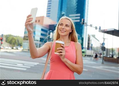 technology, lifestyle and people concept - happy smiling young woman with coffee and smartphone taking selfie on city street. woman with coffee taking selfie by smartphone