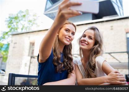 technology, lifestyle and people concept - happy young women taking selfie by smartphone and drinking coffee at cafe outdoors. young women taking selfie by smartphone at cafe