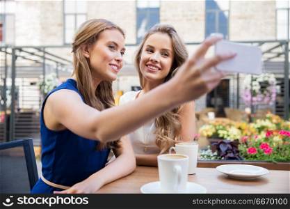 technology, lifestyle and people concept - happy young women taking selfie by smartphone and drinking coffee at cafe outdoors. young women taking selfie by smartphone at cafe. young women taking selfie by smartphone at cafe