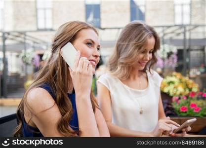 technology, lifestyle and people concept - happy young women with smartphones drinking coffee at cafe outdoors. young women with smartphones and coffee at cafe