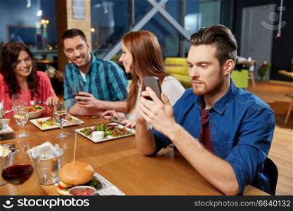 technology, lifestyle and people concept - man dining with friends and messaging on smartphone at restaurant. man messaging on smartphone at restaurant