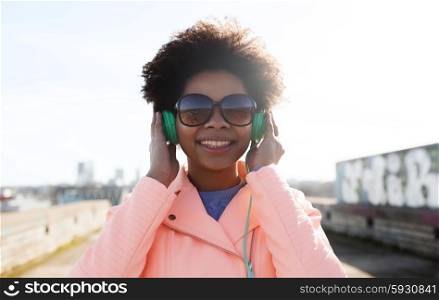 technology, lifestyle and people concept - smiling african american young woman or teenage girl in headphones listening to music outdoors