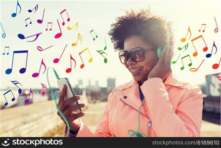 technology, lifestyle and people concept - smiling african american young woman or teenage girl with smartphone and headphones listening to music outdoors over colorful musical notes background
