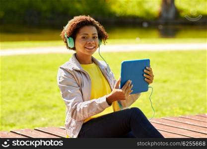 technology, lifestyle and people concept - smiling african american young woman or teenage girl with tablet pc computer and headphones listening to music in summer park