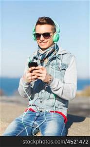technology, lifestyle and people concept - smiling young man or teenage boy in headphones with smartphone listening to music outdoors