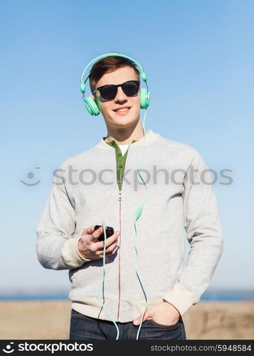 technology, lifestyle and people concept - smiling young man or teenage boy in headphones with smartphone listening to music outdoors