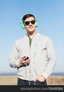 technology, lifestyle and people concept - smiling young man or teenage boy in headphones with smartphone listening to music outdoors