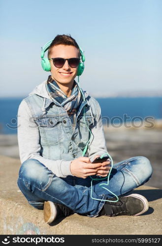 technology, lifestyle and people concept - smiling young man or teenage boy in headphones with smartphone listening to music outdoors