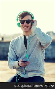 technology, lifestyle and people concept - smiling young man or teenage boy in headphones with smartphone listening to music outdoors