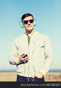 technology, lifestyle and people concept - smiling young man or teenage boy in headphones with smartphone listening to music outdoors