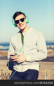 technology, lifestyle and people concept - smiling young man or teenage boy in headphones with smartphone listening to music outdoors