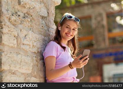 technology, lifestyle and people concept - smiling young woman or teenage girl with smartphone and earphones listening to music outdoors. happy young woman with smartphone and earphones