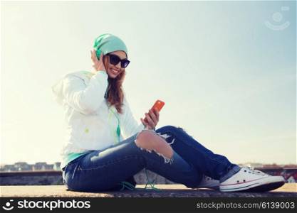 technology, lifestyle and people concept - smiling young woman or teenage girl with smartphone and headphones listening to music outdoors