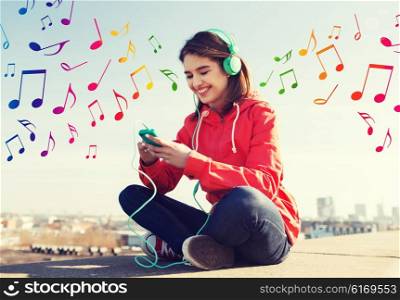 technology, lifestyle and people concept - smiling young woman or teenage girl with smartphone and headphones listening to music outdoors over colorful musical notes background