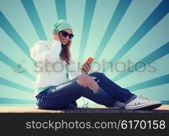 technology, lifestyle and people concept - smiling young woman or teenage girl with smartphone and headphones listening to music over blue burst rays background