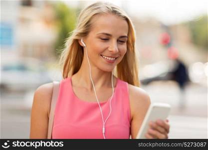 technology, lifestyle and people concept - smiling young woman with smartphone and earphones listening to music in city. happy young woman with smartphone and earphones