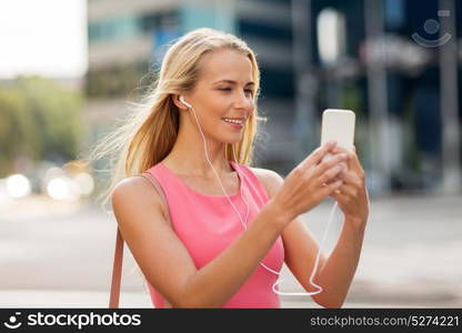 technology, lifestyle and people concept - smiling young woman with smartphone and earphones listening to music and taking selfie in city. happy young woman with smartphone and earphones