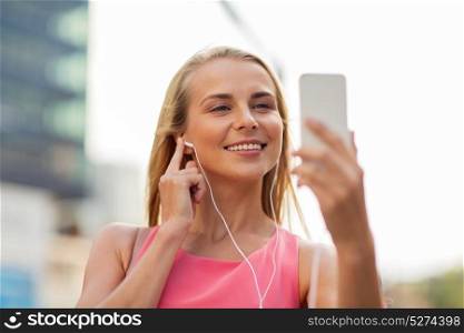technology, lifestyle and people concept - smiling young woman with smartphone and earphones listening to music and taking selfie in city. happy young woman with smartphone and earphones