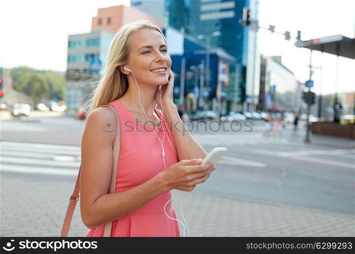 technology, lifestyle and people concept - smiling young woman with smartphone and earphones listening to music in city. happy young woman with smartphone and earphones