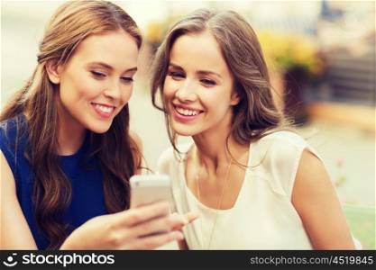 technology, lifestyle, friendship and people concept - happy young women or teenage girls with smartphone at outdoor cafe