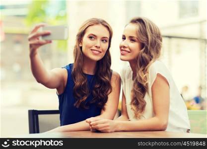 technology, lifestyle, friendship and people concept - happy young women or teenage girls with smartphone taking selfie at outdoor cafe