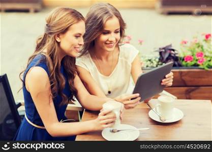 technology, lifestyle, friendship and people concept - happy young women or teenage girls with tablet pc computer drinking coffee at outdoor cafe