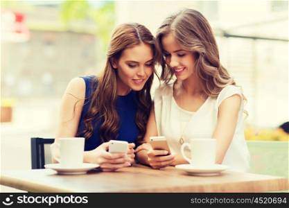 technology, lifestyle, friendship and people concept - happy young women or teenage girls with smartphones and coffee cups at cafe outdoors