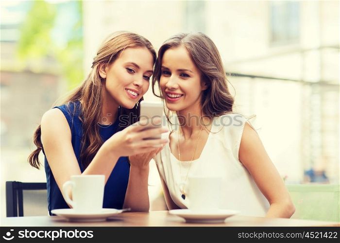 technology, lifestyle, friendship and people concept - happy young women or teenage girls with smartphone and coffee cups at outdoor cafe