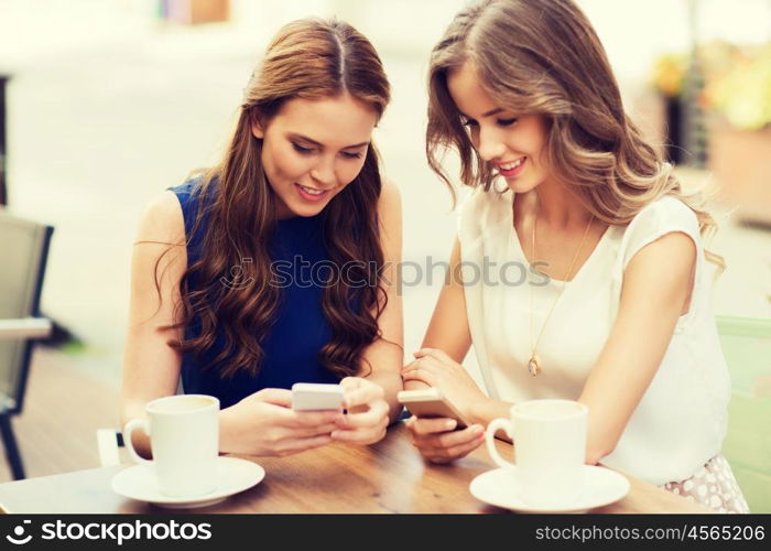 technology, lifestyle, friendship and people concept - happy young women or teenage girls with smartphones and coffee cups at cafe outdoors