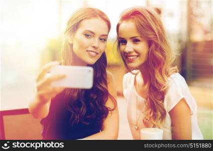 technology, lifestyle, friendship and people concept - happy young women or teenage girls with smartphone and coffee cups taking selfie at outdoor cafe. happy women with smartphone taking selfie at cafe
