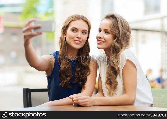 technology, lifestyle, friendship and people concept - happy young women or teenage girls with smartphone taking selfie at outdoor cafe