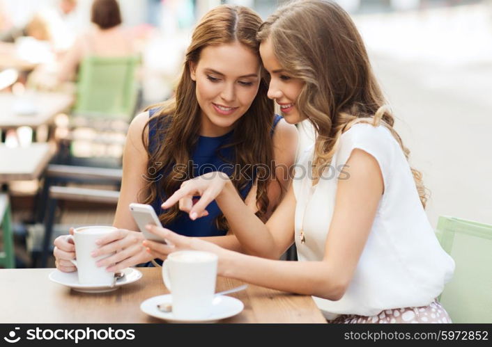 technology, lifestyle, friendship and people concept - happy young women or teenage girls with smartphone and coffee cups at outdoor cafe