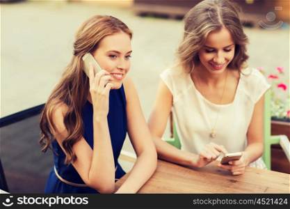 technology, lifestyle, friendship, communication and people concept - happy young women or teenage girls with smartphones at cafe outdoors