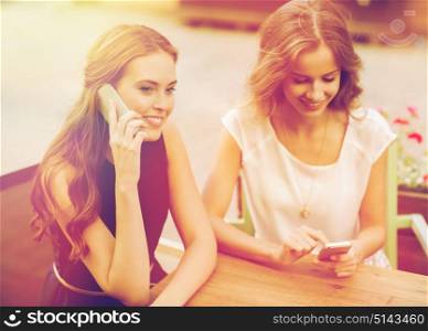 technology, lifestyle, friendship, communication and people concept - happy young women or teenage girls with smartphones at cafe outdoors. happy young women with smartphones at outdoor cafe