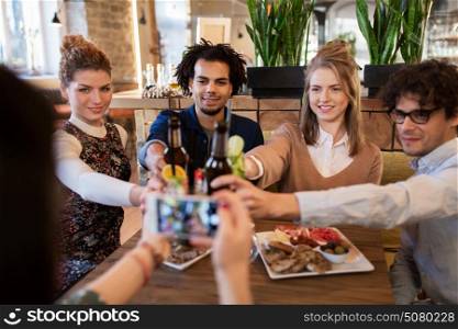 technology, lifestyle, holidays and people concept - happy friends clinking drinks and photographing by smartphone at bar or cafe. happy friends clinking drinks at bar or cafe