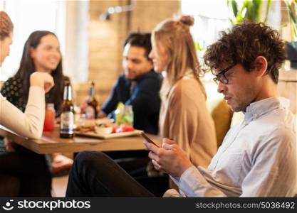 technology, lifestyle, holidays and people concept - man with smartphone and friends at restaurant. man with smartphone and friends at restaurant