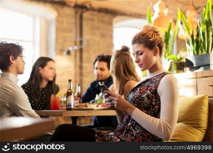 technology, lifestyle, holidays and people concept - woman with smartphone and friends at restaurant. woman with smartphone and friends at restaurant