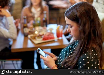 technology, lifestyle, holidays and people concept - woman with smartphone and friends at restaurant. woman with smartphone and friends at restaurant
