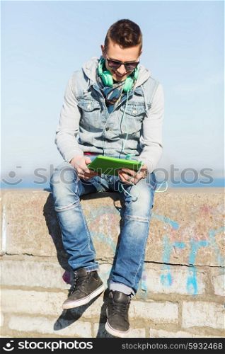 technology, lifestyle, music and people concept - smiling young man or teenage boy with tablet pc computer and headphones outdoors