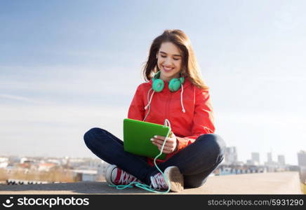 technology, lifestyle, music and people concept - smiling young woman or teenage girl with tablet pc computer and headphones outdoors